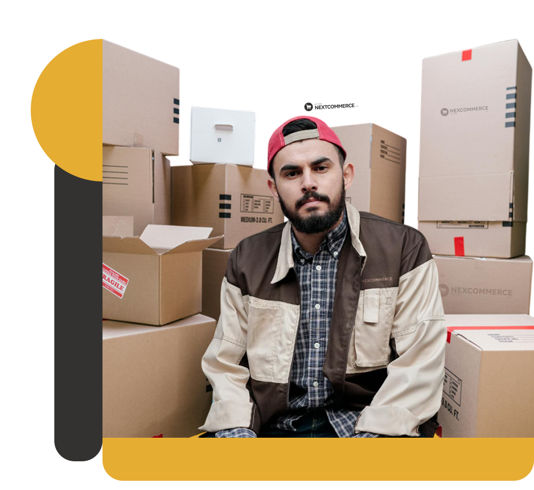 Warehouse worker in Nexcommerce uniform sitting in front of stacked cardboard boxes, some marked fragile.